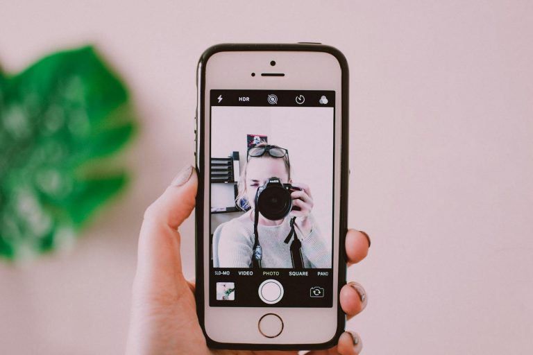 A person taking a selfie with a camera through a smartphone, showing a creative reflection.