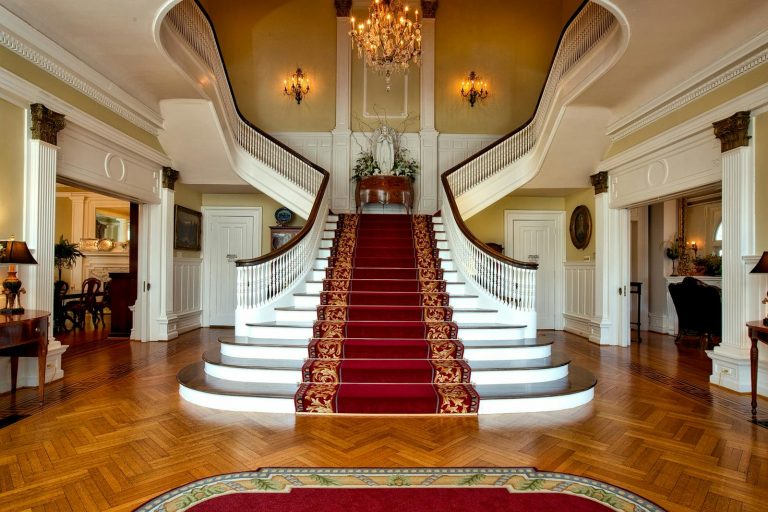 Grand staircase with red carpet in a luxurious hotel lobby, highlighted by a chandelier.