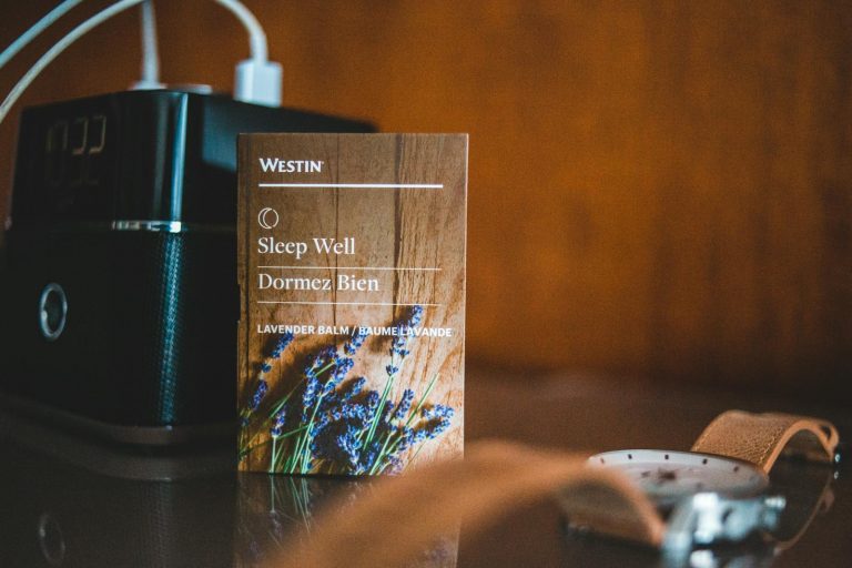 A nightstand featuring a lavender sleep aid card, a classic wristwatch, and speakers for a relaxing atmosphere.